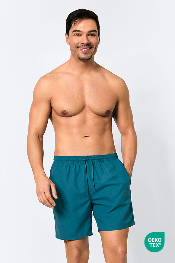 Männermodel trägt blaue Badeshorts.