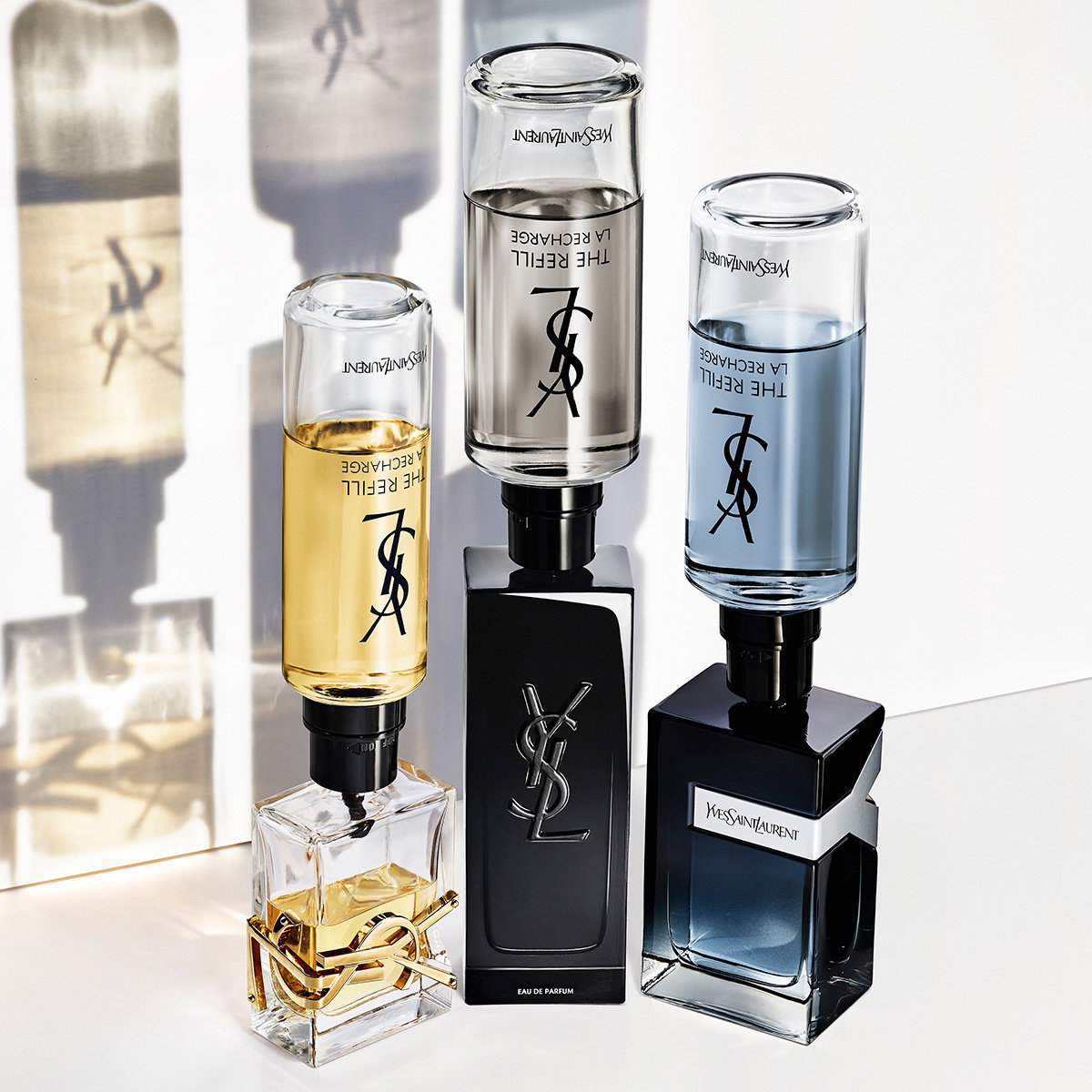 Three different YSL fragrance bottles—Libre, MYSLF, and Y—being refilled simultaneously with upside-down refill bottles.