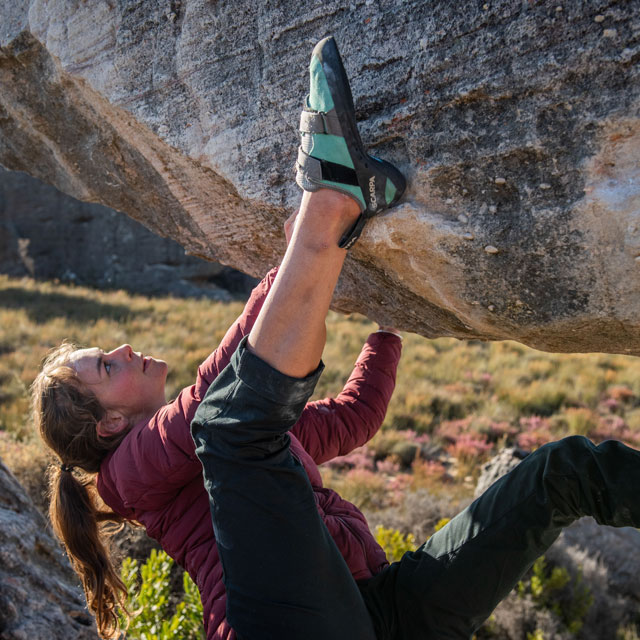 A woman climbing with her heel hooked around the rock face.