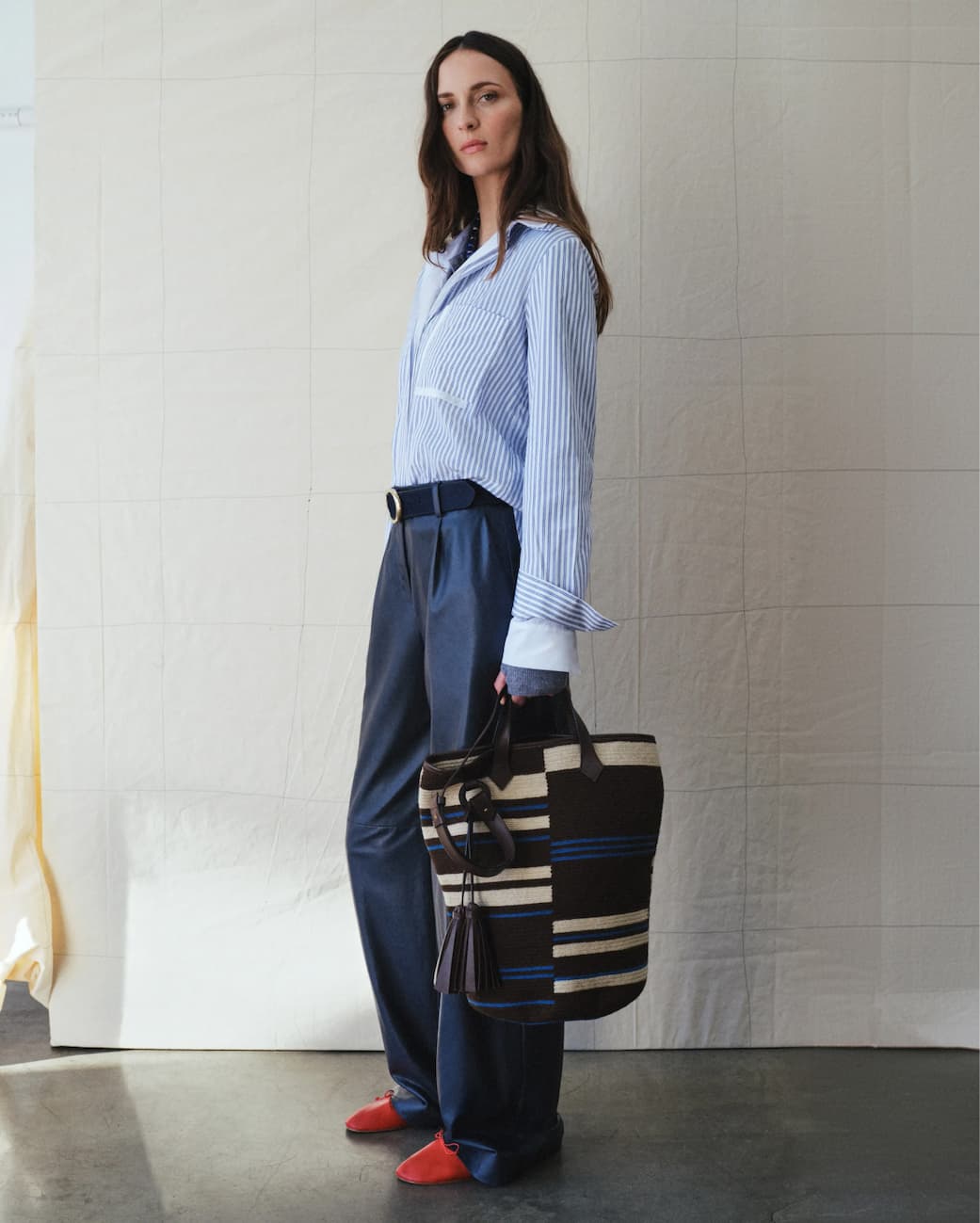 Image of a model in a blue striped top and blue pants and a woven bag.