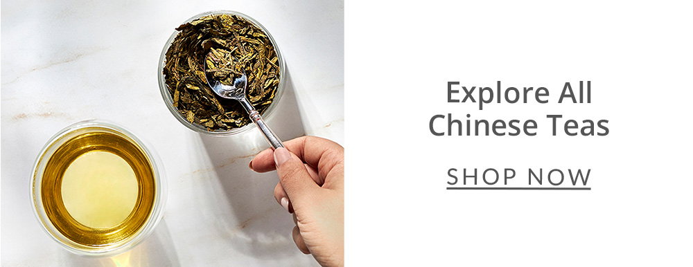 Chinese green loose leaf tea in a bowl with a hand holding a silver spoon scoop tea with a cup of green tea next to it
