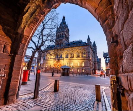 View of a historic building illuminated at dusk, framed by an archway and cobblestone street.