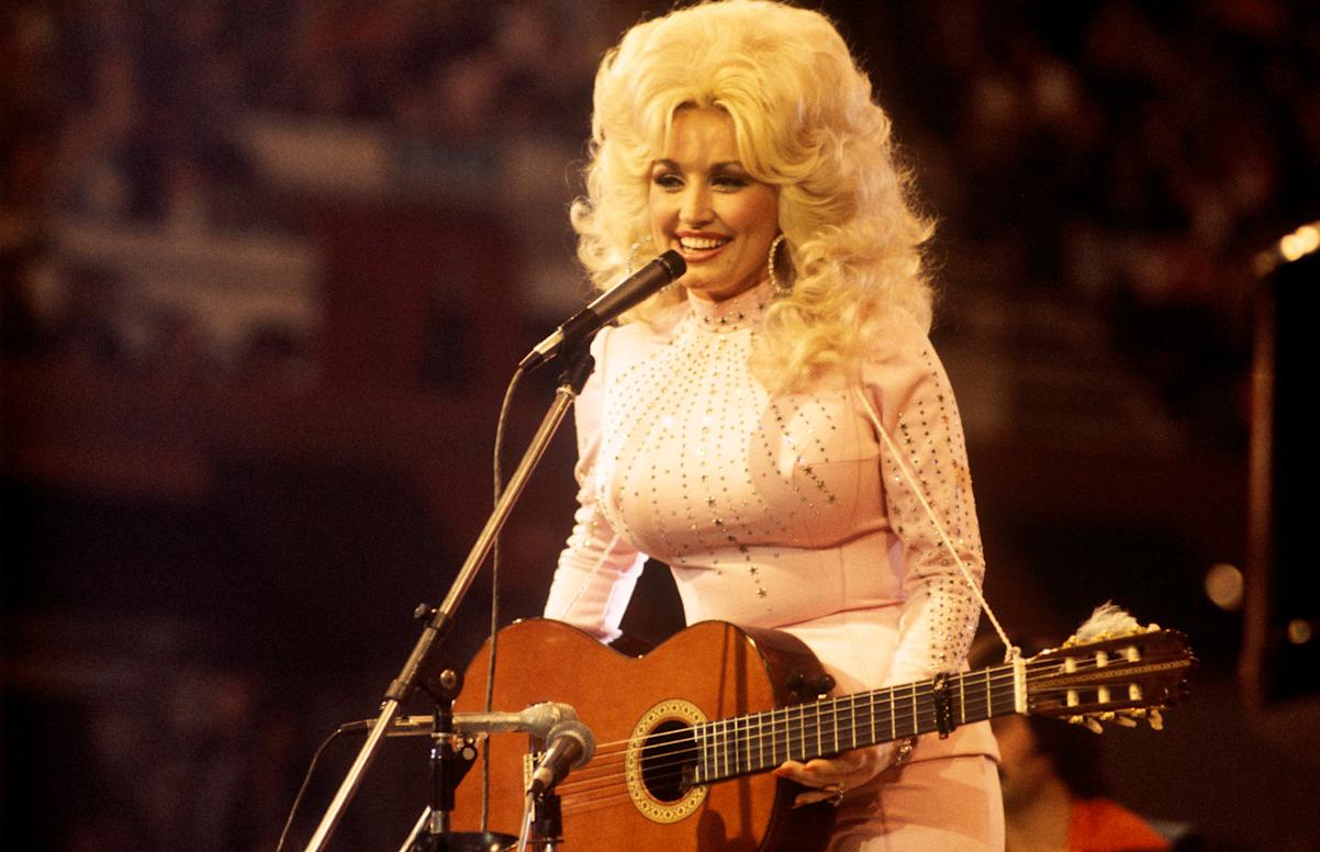 Dolly Parton, performs with a guitar, 1976