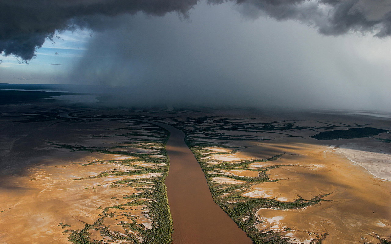 Monsoon rains over a muddy river in Wyndham, Western Australia. During monsoon season, the continent warms faster than the ocean, pulling in moist winds that cause widespread heavy rain and thunderstorms.