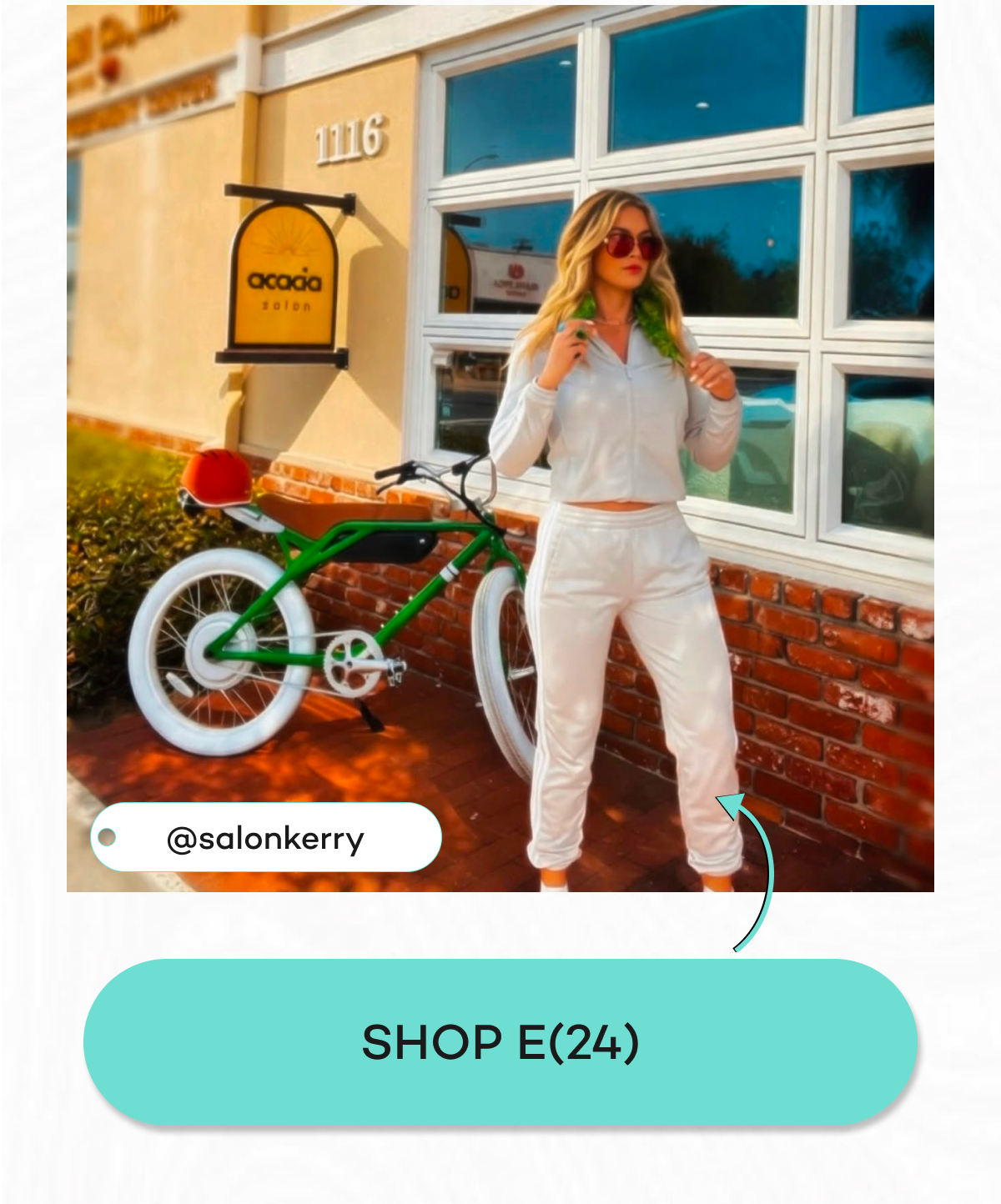 A woman in a white tracksuit stands next to a green e(24) bicycle outside a salon.