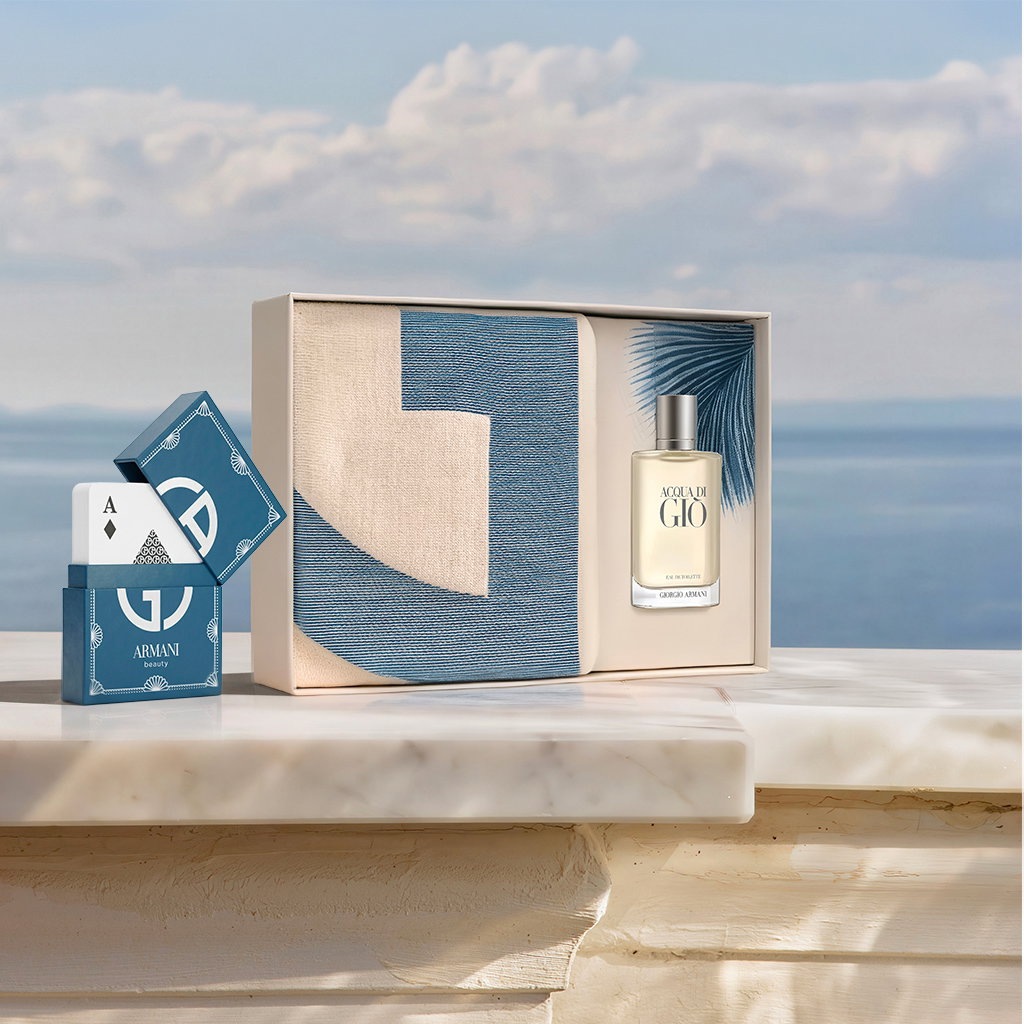 An elegant Armani gift box adorned with blue palm leaf motifs, set on a sun-drenched marble surface with a magnificent view of the ocean in the background.