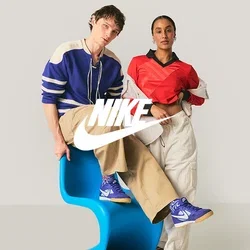 Twee jonge volwassenen in casual kleding poseren; de een zit op een blauwe moderne stoel, de ander staat met een hand in de zak tegen een effen achtergrond.