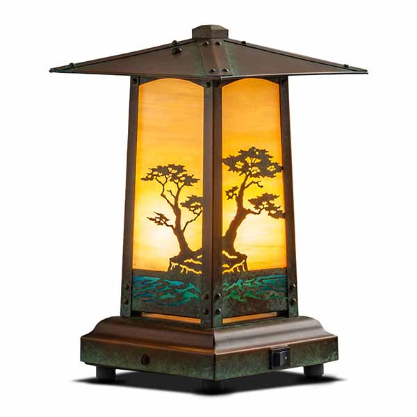 A glowing table lamp with tree artwork.