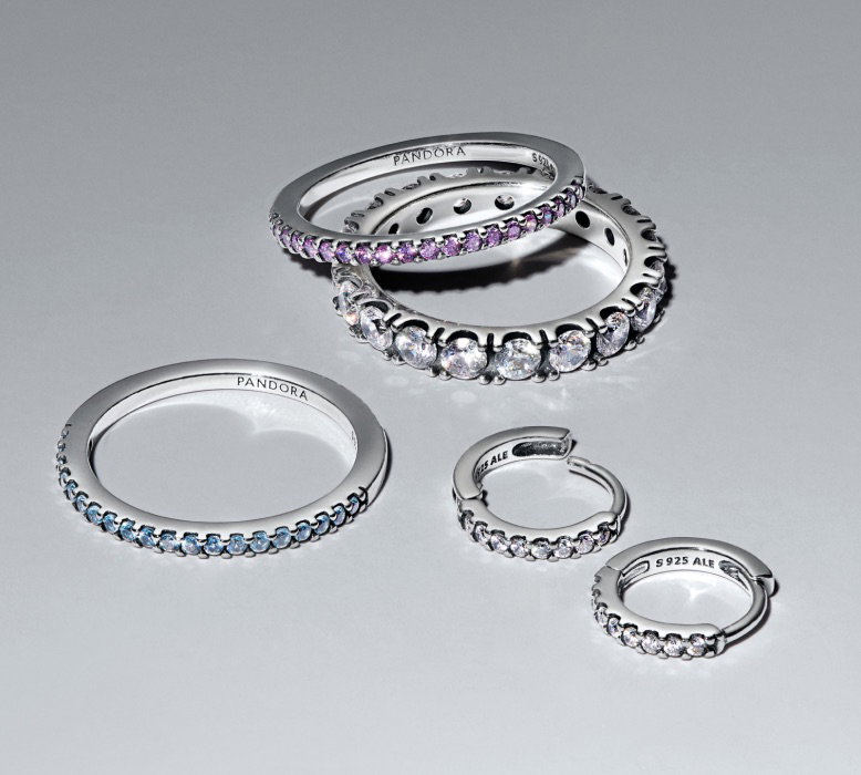 Sterling silver Pandora Timeless rings and hoops scattered on a grey background.