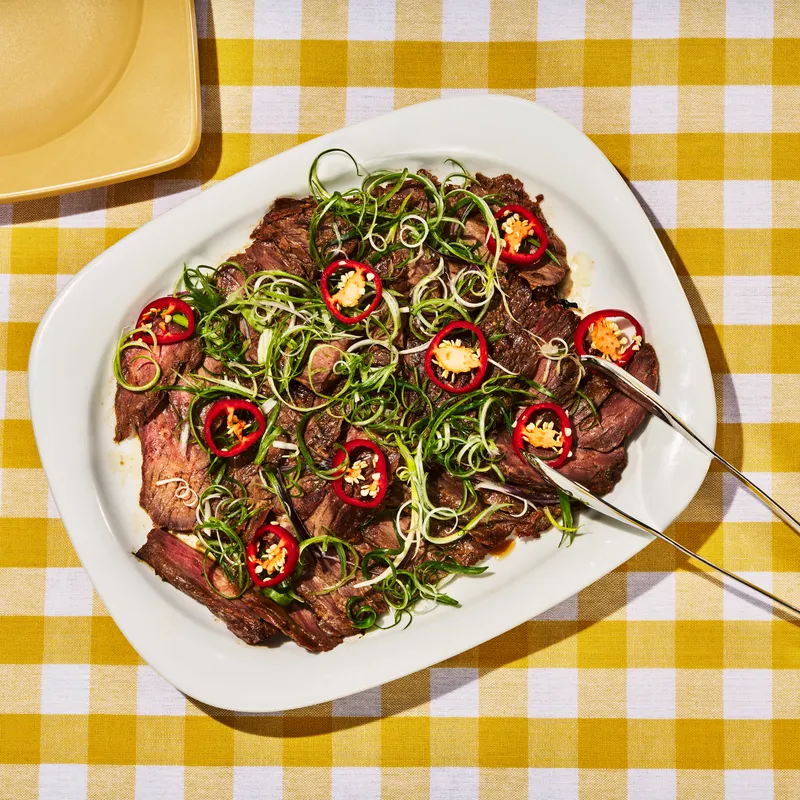 Soy-And-Cola-Marinated Steak on a rectangular platter with tongs to the side