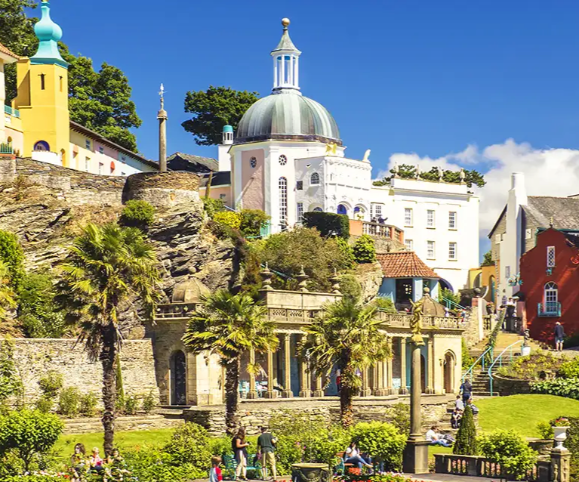 A vibrant coastal scene featuring colourful buildings, palm trees, and lush greenery under a blue sky.