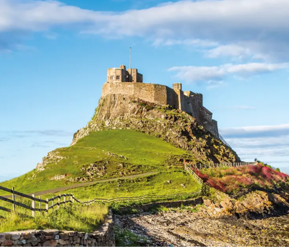 A historic castle atop a grassy hill, surrounded by blue skies and a winding path.