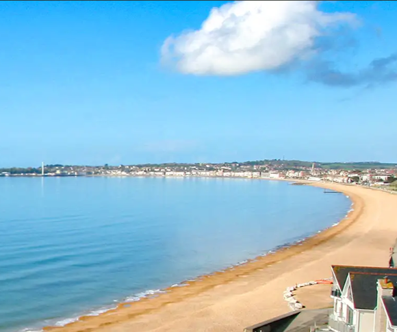 A serene beach scene with calm waters, sandy shore, and a clear blue sky.