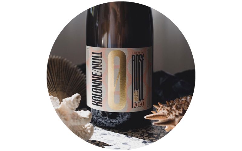 Close-up of a Kolonne Null non-alcoholic rosé bottle (2020) on a patterned surface with decorative seashells