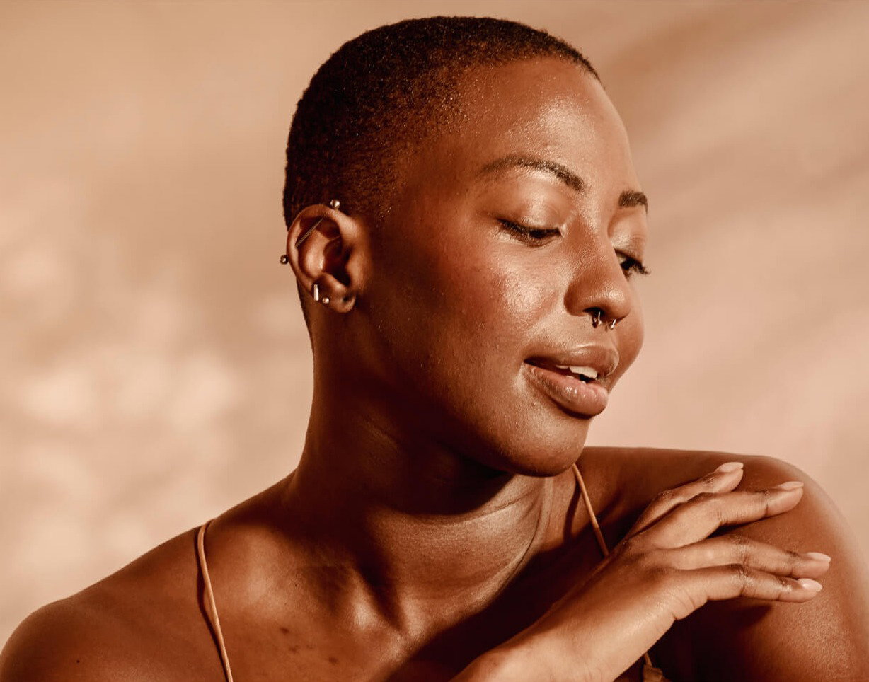Close-up portrait of a woman with glowing, healthy skin against a warm neutral background