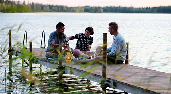 Drei Menschen sitzen auf einem Steg am See in Finnland.