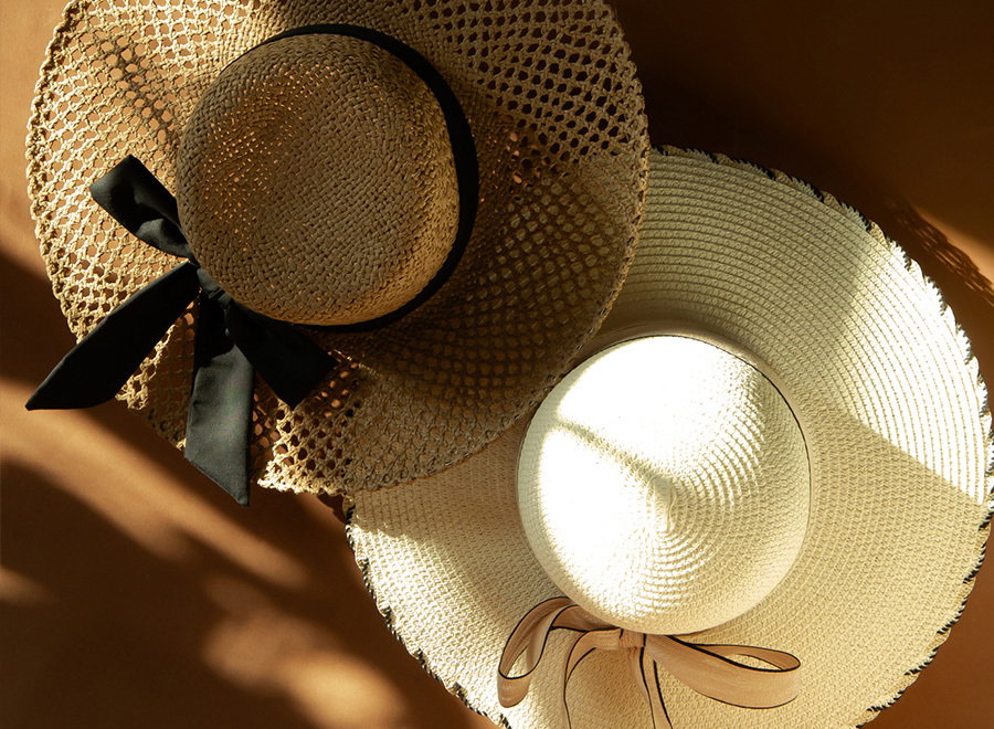 Two straw hats with ribbons, one black and one beige, on a brown background