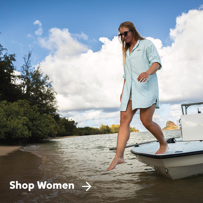 Woman stepping from boat to beach while wearing long Columbia shirt.