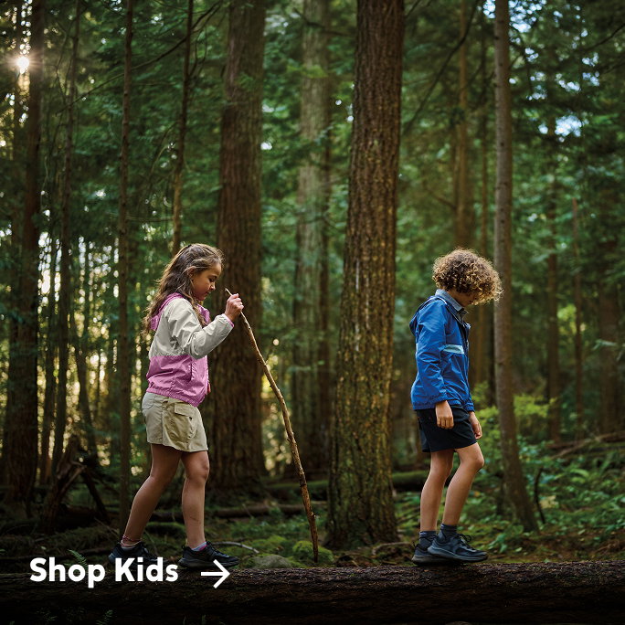 Two kids hiking a trail, little girl behind the boy has a hiking stick.