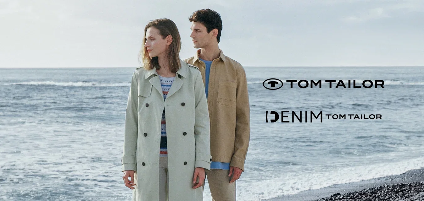 Hellgrüner Trenchcoat, beiges Hemd, weiße Hose und braune Schuhe. Beide Kleidungsstücke sind lässig, mit weichen Texturen vor einer felsigen Strandkulisse.