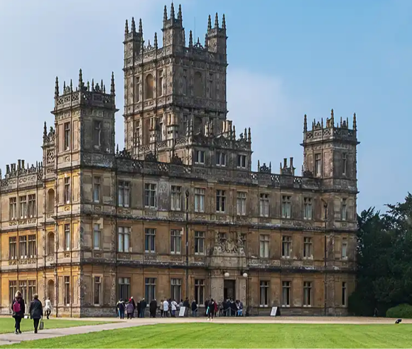 A grand historic mansion with intricate architecture and visitors in the foreground on a grassy lawn.