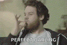 a man with a beard is blowing a kiss while sitting on a couch and says `` perfect darling '' .