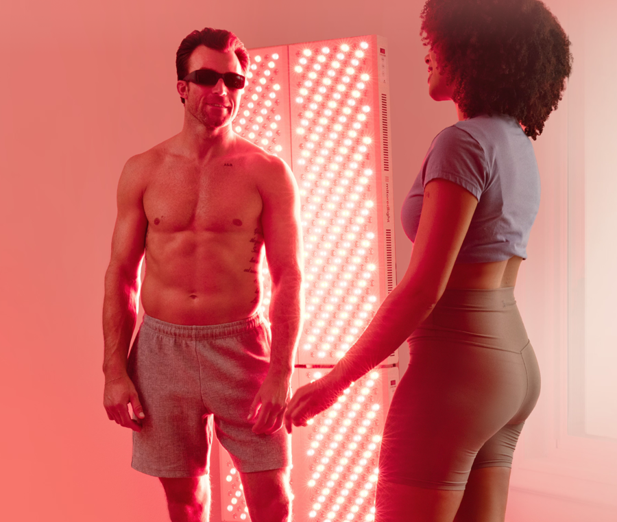 Man and woman stand in front of red light therapy panel.