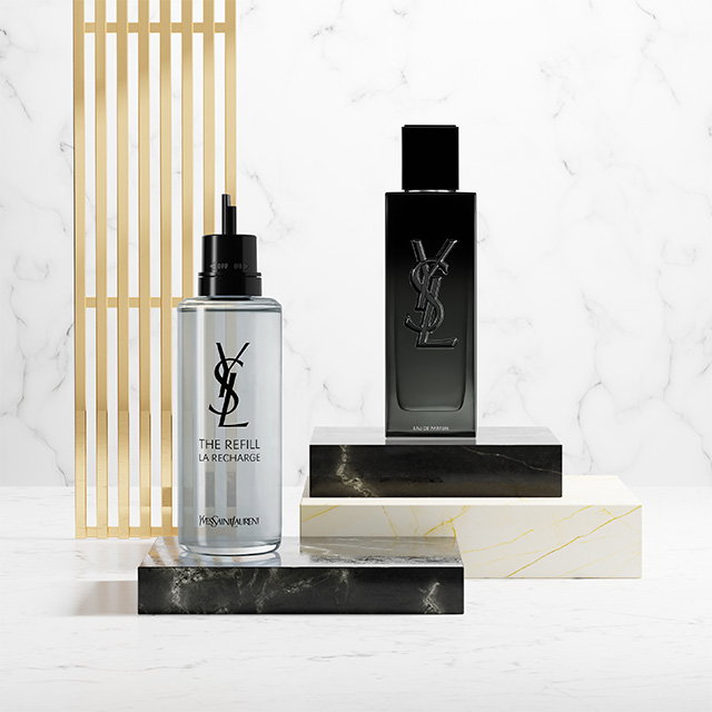 A black YSL MYSLF fragrance bottle and its metallic refill bottle displayed on marble and black stone pedestals.