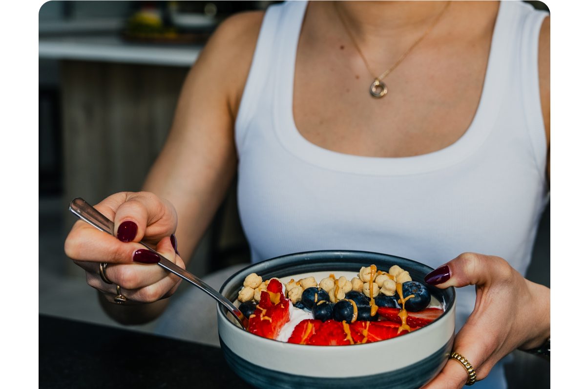 A person holding a bowl of yogurt topped with strawberries, blueberries, and granola.