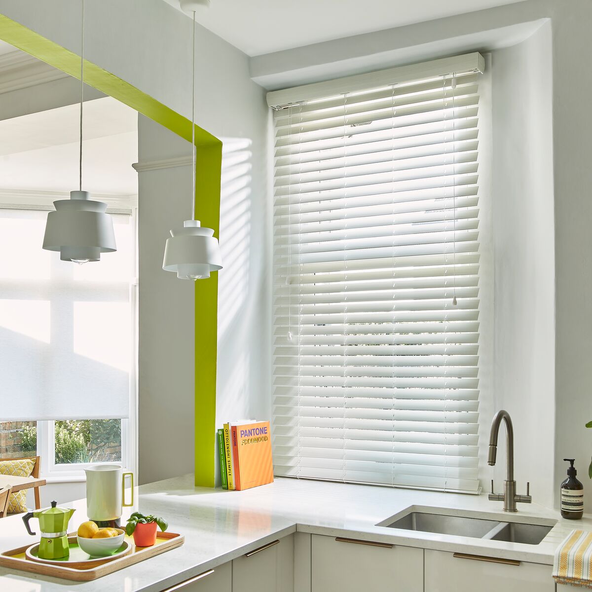 A kitchen window fitted with white wooden Venetian blinds with horizontal slats