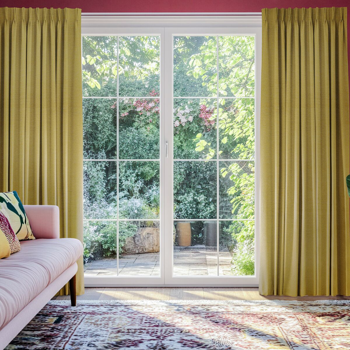 Pencil pleat mustard yellow curtains pushed to either side of large glass patio doors opening to a garden