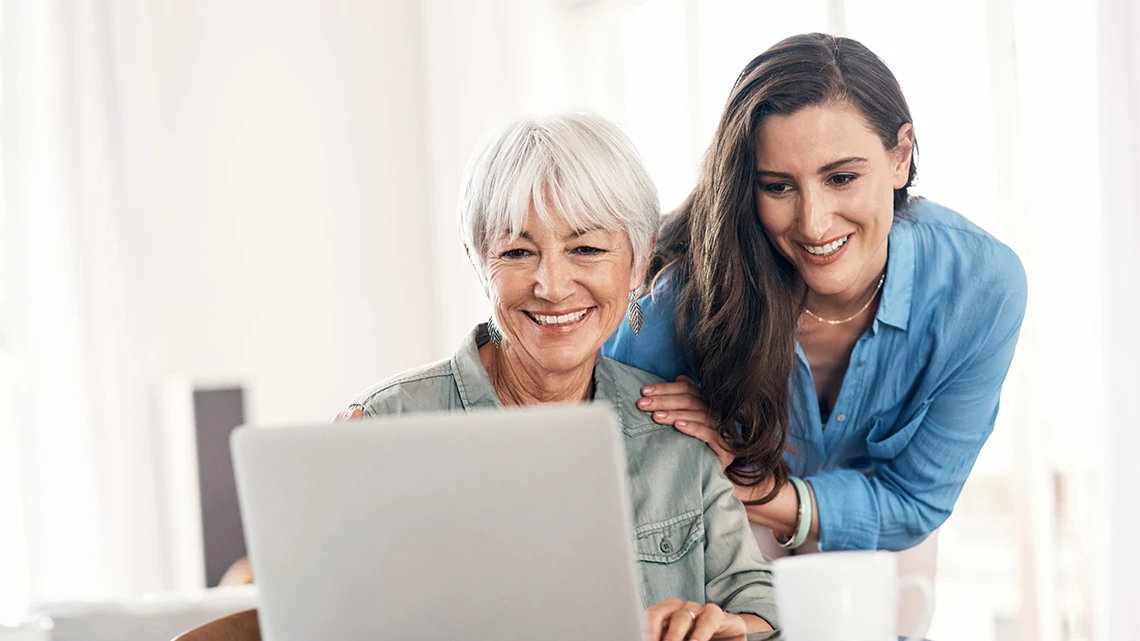 woman with white short hair looking at laptop while woman with long brown hair stands over her shoulders looking at what is on screen