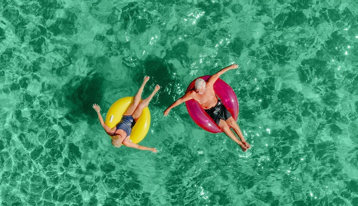 Overhead photo of a couple on vacation floating on inflatable rings in the sea with blue water