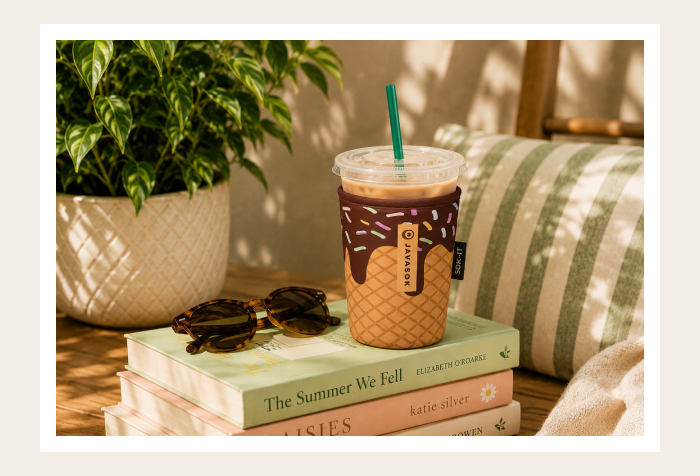 Iced coffee tumbler on stacked books with sunglasses.