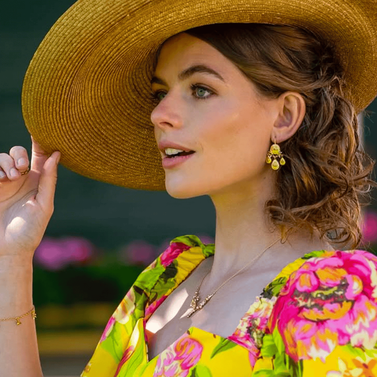 Rosie Tapner wearing Alex Monroe Gratitude for Nature Girandole Earrings and necklace with a wide-brim straw hat and floral dress.