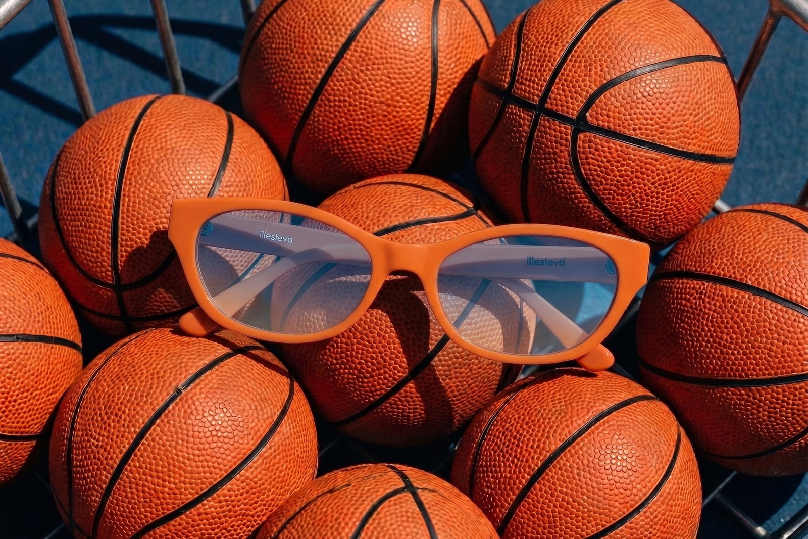 Encinitas sunglasses in Aperol with Blue Gradient See Through on top of a container of basketballs