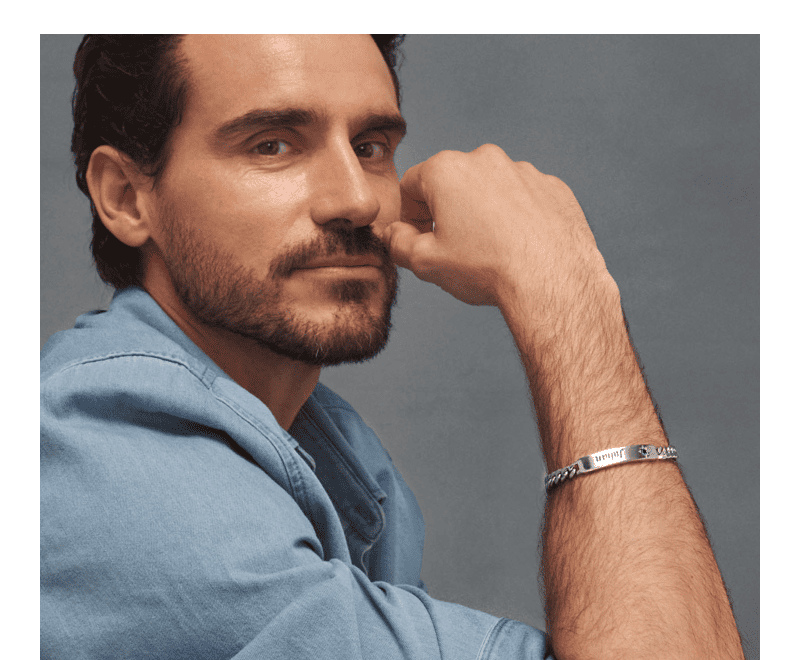 Man in blue shirt wearing a silver chain bracelet with engraved plate and curb links. 