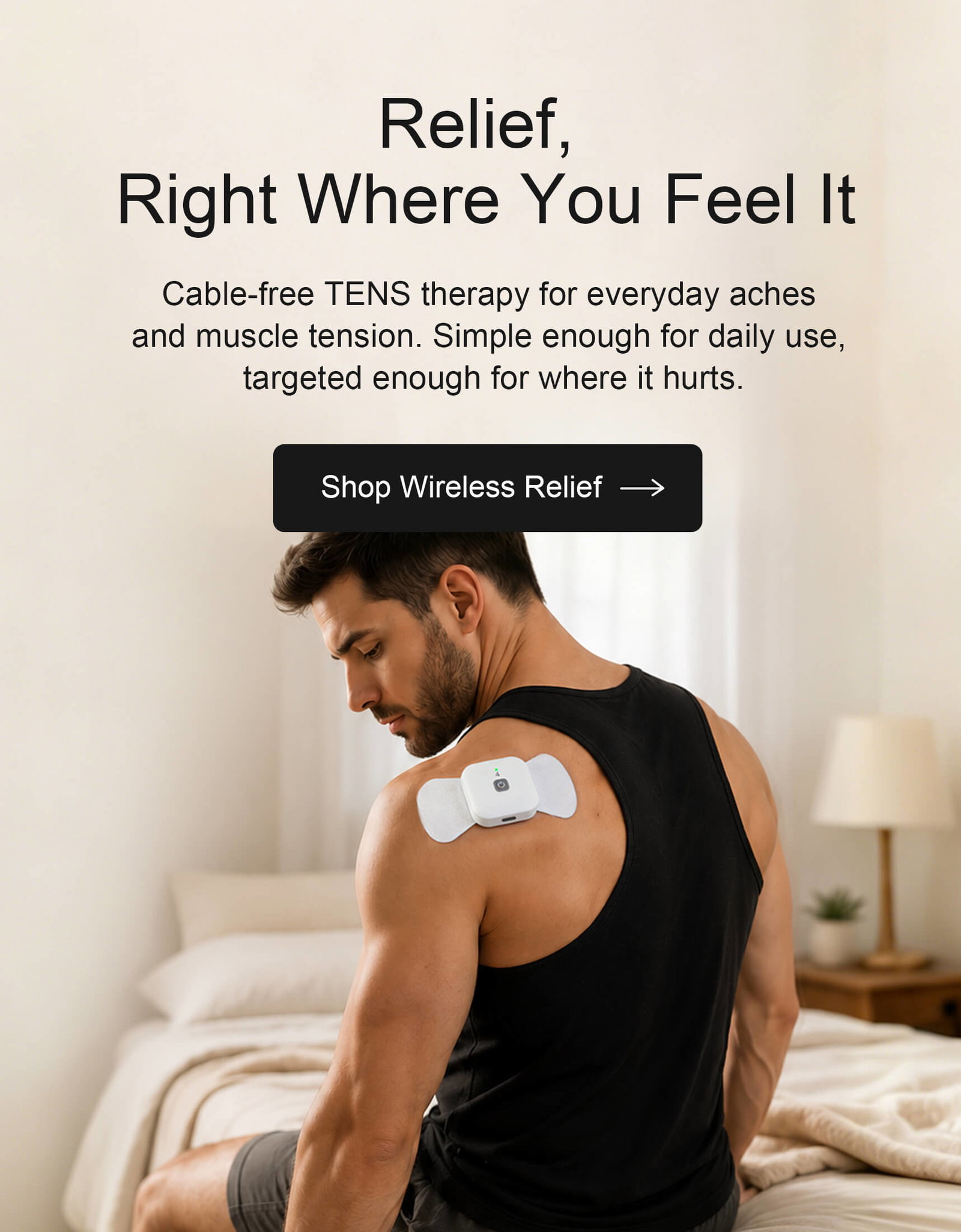 Man using a wireless TENS therapy device on his shoulder while sitting in a warm bedroom setting.