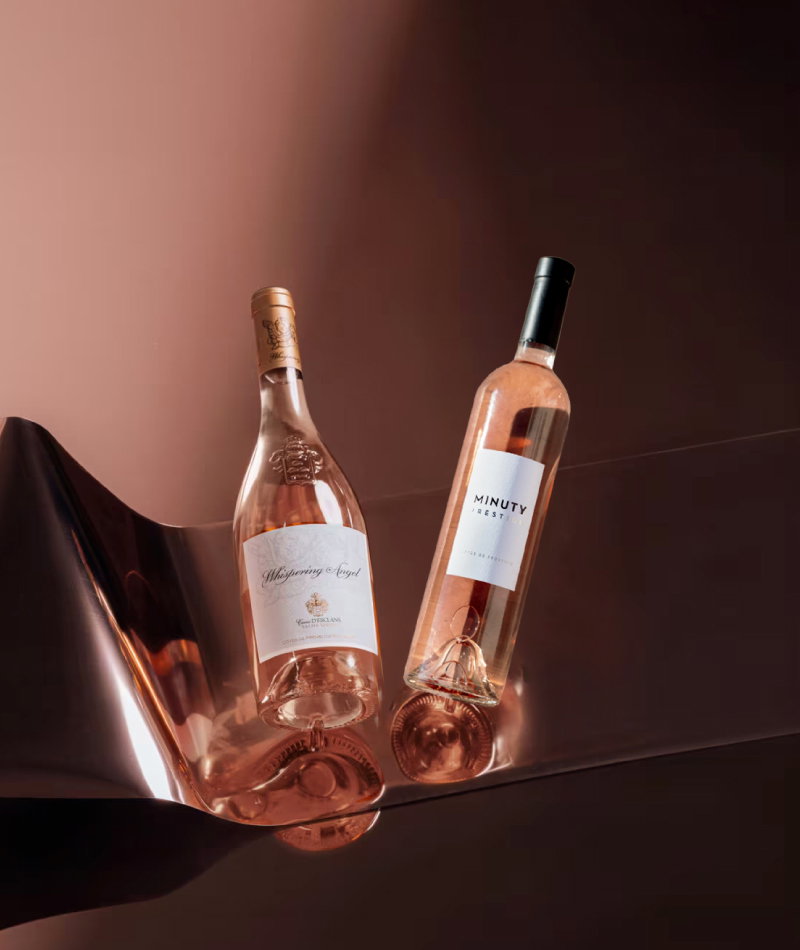 Two rosé wine bottles with white labels reflected on a glossy copper surface, elegant product photography