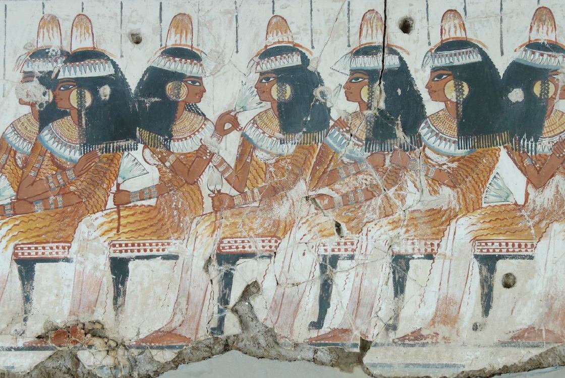 Detail of an ancient Egyptian wall painting showing a row of women seated at a banquet, wearing wigs, elaborate jewellery, and perfume cones while holding lotus flowers.