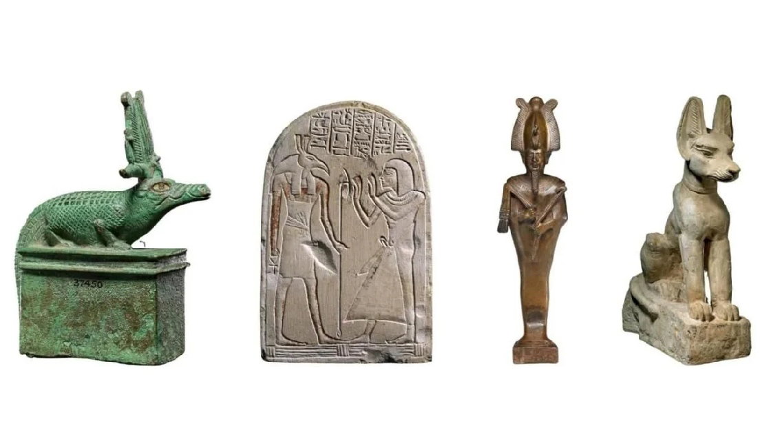 From left to right: a green, bronze crocodile figure, a carved limestone with hieroglyphs and two figures carved on it, a copper human figure and a limestone sculpture of a jackal.