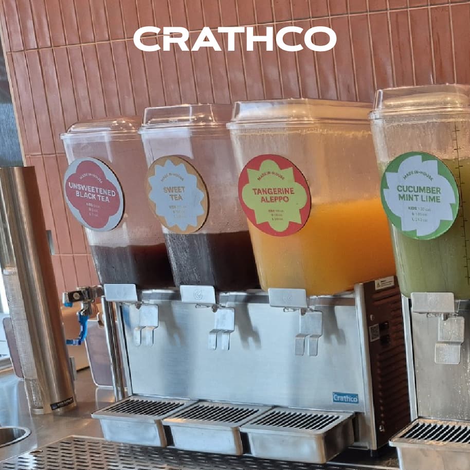 Crathco multi‑tank beverage dispenser labeled with unsweetened black tea, sweet tea, tangerine, and cucumber mint lime drinks on a countertop.