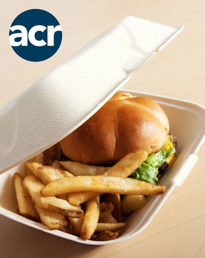 ACR hinged takeout container holding a cheeseburger and fries with the lid partially open on a tabletop.