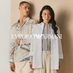 Twee mensen staan tegen een beige paneel, één draagt een shirt met patroon en crèmekleurige broek, de ander een witte blazer en losse crèmekleurige broek.