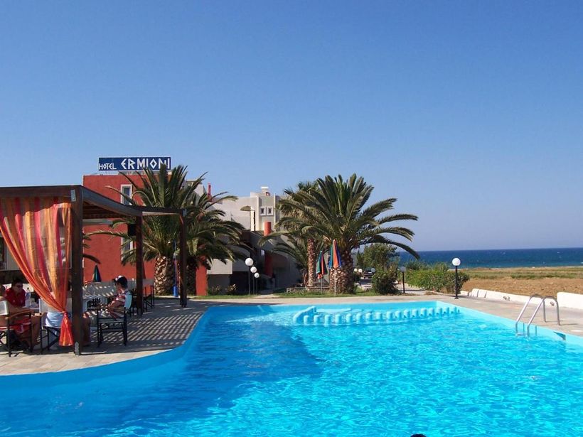 Sunlit hotel swimming pool with palm trees, sea view and shaded poolside dining area