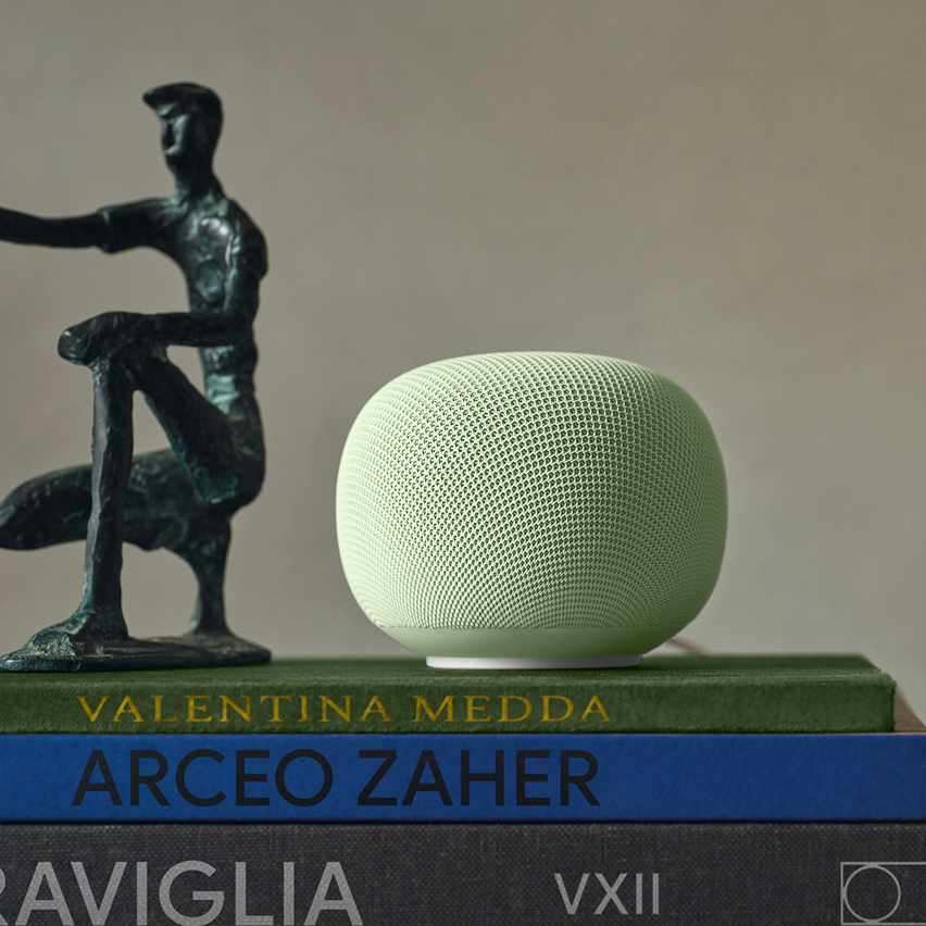 Green smart speaker on a stack of books beside a bronze abstract sculpture.