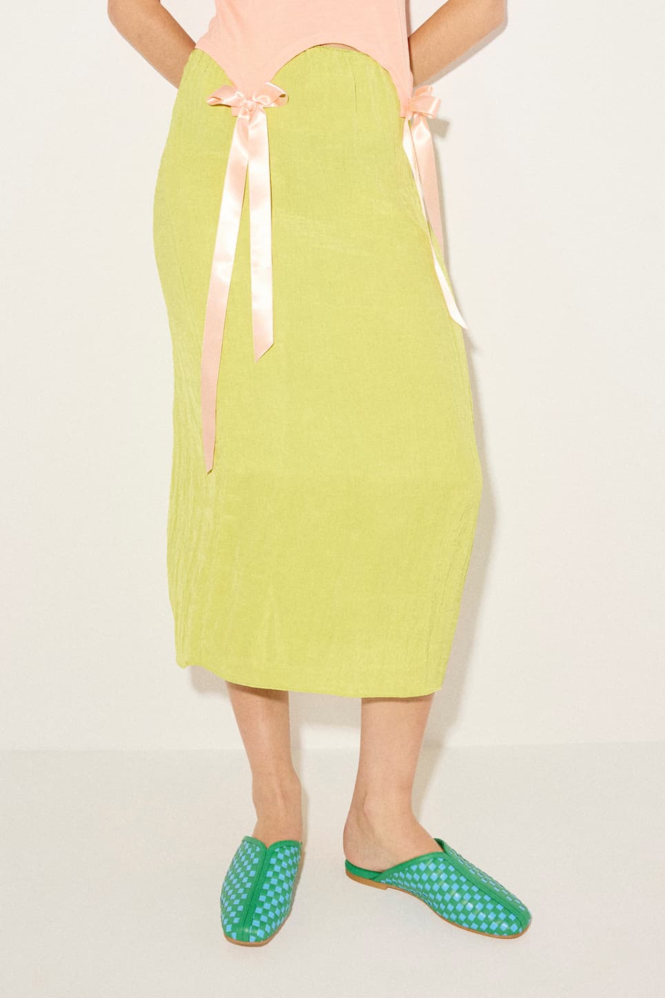 woman in neon yellow skirt with pink ribbon wearing green and blue woven slides