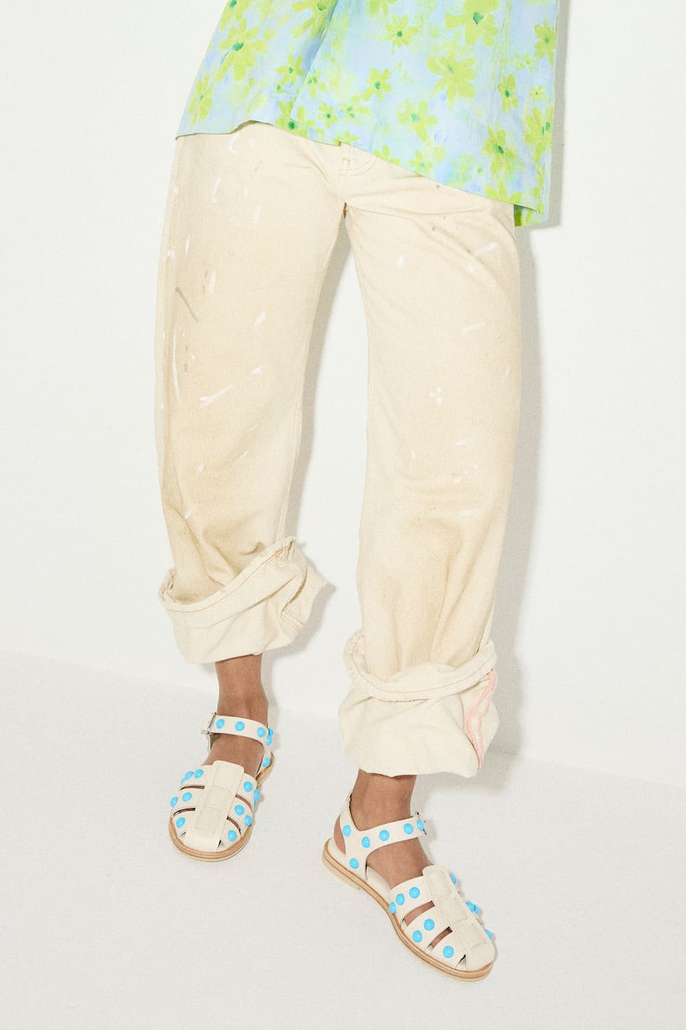 woman in blue and green floral top with cuffed khaki pants with white pant splatters wearing bone colored sandals with blue studs