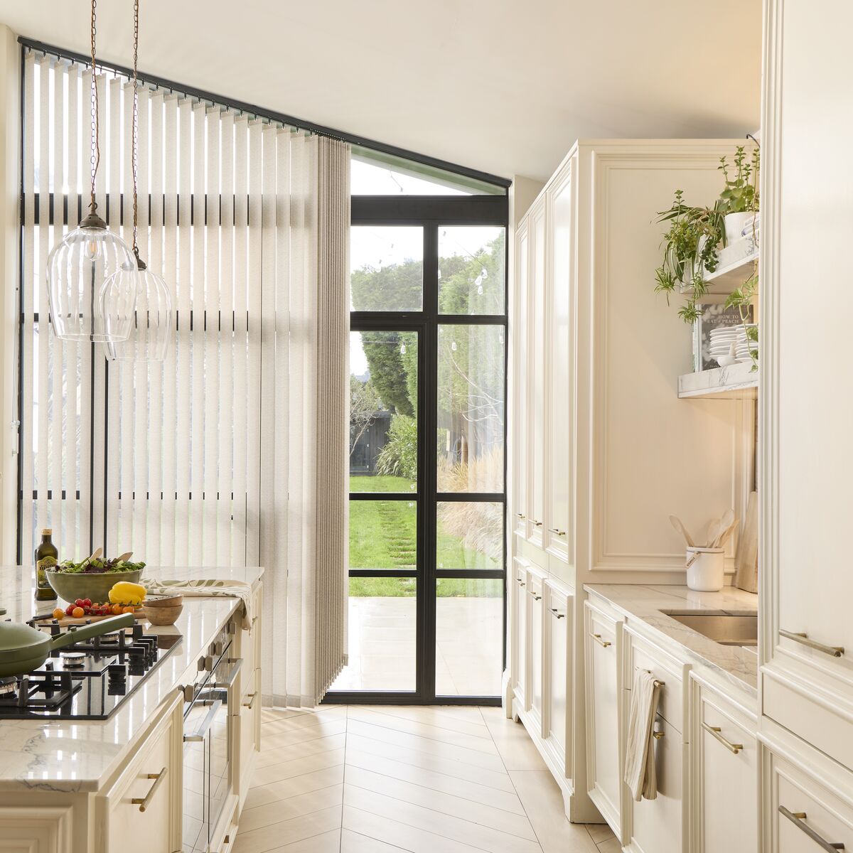 Dining room with wide window dressed in soft blue Vertical blinds, filtering daylight over a wooden table set with ceramics and greenery.