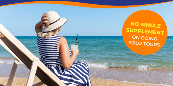 A woman in a striped dress relaxes on a beach chair, enjoying a drink by the sea.